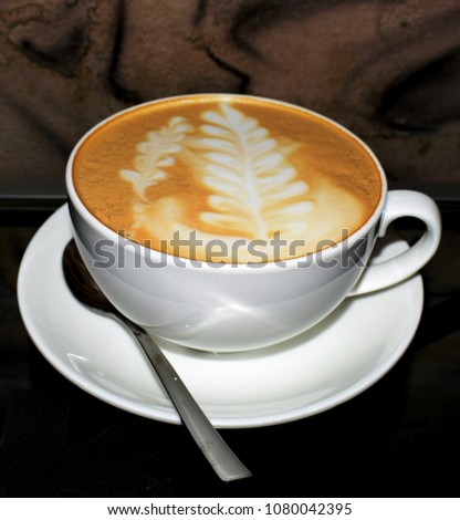 Photo of a white cup with coffee. A picture in the form of a twig on a cappuccino.