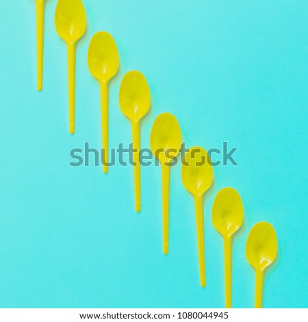 yellow plastic spoons in line on turquoise background. minimal art