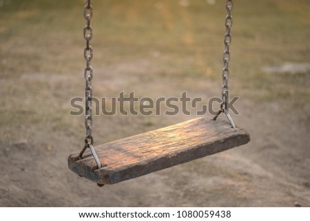 Wooden swings are hung by chains in the playground evening.