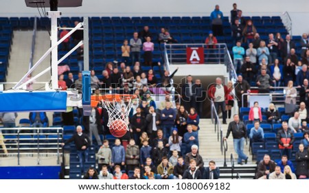 The basketball ball flies through the basket. In the background, fans are sitting in the stands
