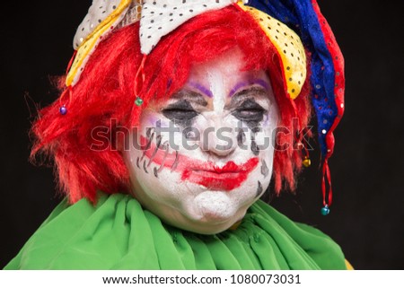 A horrible clown with a terrible make-up and hat on his head laughing on a black background