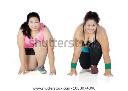 Picture of two obese women ready to compete while kneeling together in the studio, isolated on white background