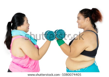 Picture of two fat women wearing sportswear while doing a workout together and lifting barbells, isolated on white background