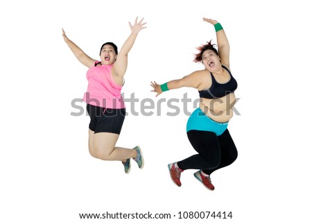 Picture of two young fat women looks happy while jumping together in the studio, isolated on white background