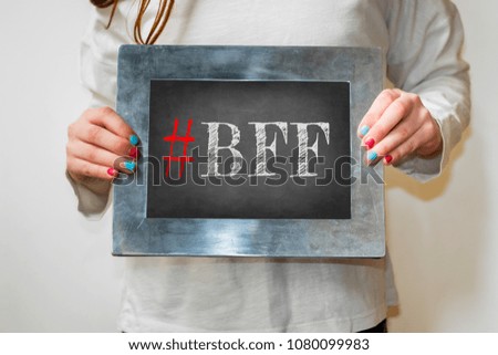 Young girl holding up blackboard with text #BFF