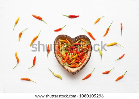 Colorful chili peppers in wooden dish heart shape on white.