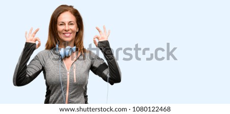 Middle age gym fit woman with workout headphones doing ok sign gesture with both hands expressing meditation and relaxation isolated blue background