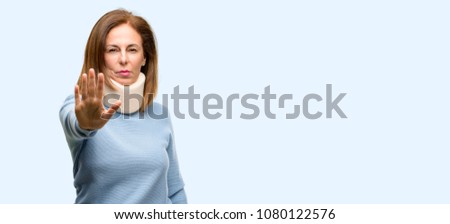 Injured woman wearing neck brace collar annoyed with bad attitude making stop sign with hand, saying no, expressing security, defense or restriction, maybe pushing isolated blue background