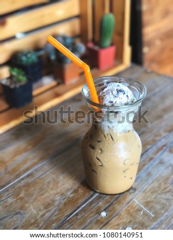 ice coffee topped with chocolate chip ice cream and orange strew in glass on vintage wooden table, ice coffee float glass with cactus background