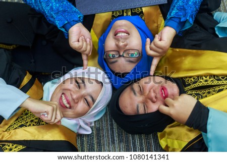 Happy women students in graduation dress lay down on floor. Friendship, success, educational concept. 