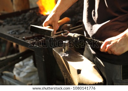 The blacksmith works with anchor metal on an anvil with a hammer and ticks
