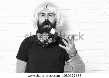 handsome bearded man with stylish mustache in pink wig with colorful autumn flowers in long beard on funny face on white brick wall background