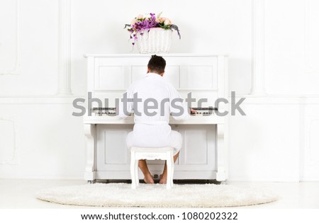 Man in bathrobe enjoys morning while playing piano. Talented musician concept. Man sleepy in bathrobe sit in front of piano musical instrument in white interior on background, rear view.