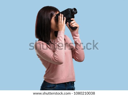 Young pretty woman excited and entertained, looking through a film camera, looking for an interesting shot, recording a movie, executive producer