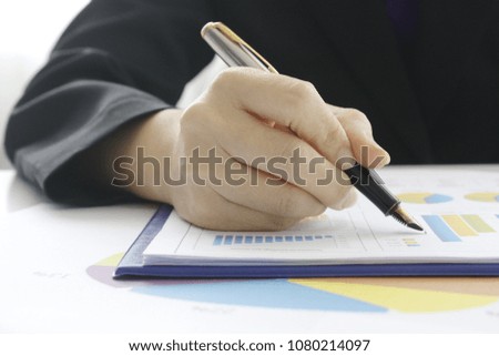 Businesswoman holding pen with graph 
lose up of woman's hand writing in notepad placed on desktop with other 