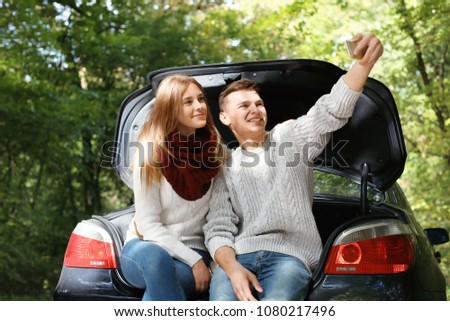 Happy young couple taking selfie near car outdoors