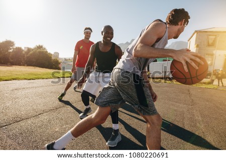 Men playing basketball game on a sunny day. Men practicing basketball skills in play area.