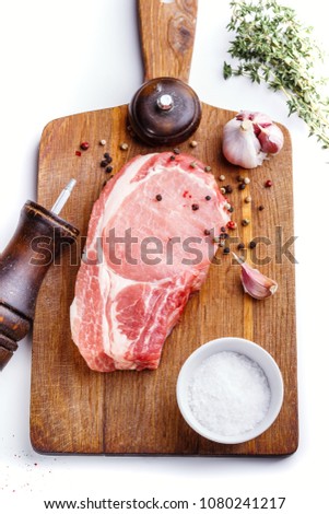 Raw pork natural cutlet with twigs of thyme, garlic, pepper and a pepper mill with a cutting board. Top view. Royalty-Free Stock Photo #1080241217