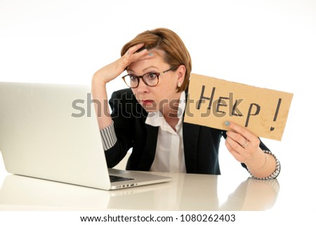 beautiful young red haired caucasian tired and frustrated business woman working on her computer holding a help sign at work office desk on a white background.Stress and business frustration concept