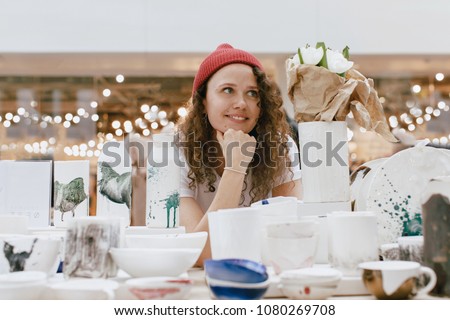 Young hipster woman selling behind counter with her ceramics and porcelain hand-painted at local market of craftsmen, small business