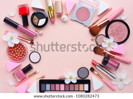 Makeup brush and decorative cosmetics with apple blossom arranged around a blank space on a pastel pink background. Top view