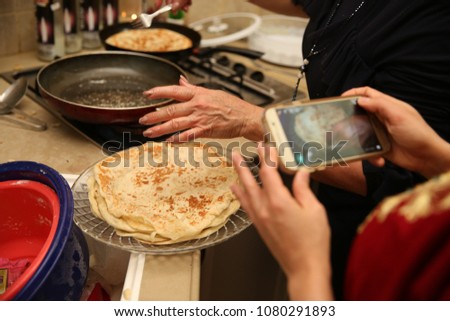 Hand places the Jewish ethnic food called 'mufleta' on a platter while someone takes a cell phone picture. This food is traditionally made at the end of the Passover holiday