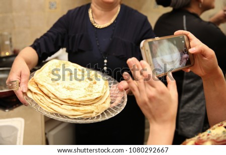 Woman holds the Jewish ethnic food called 'mufleta' on a platter while someone takes a cell phone picture. This food is traditionally made at the end of the Passover holiday