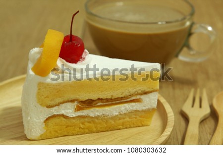 a piece of cake with red sherry on top on wooden plate and a cup of coffee on wooden table.