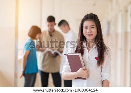 Education learning Concept: Confident Asian Students Cute girl holding books, smiling at camera at Outside classroom at university with blur young mans her friend background