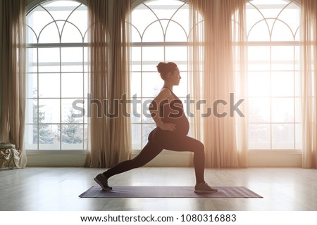 Pregnant Woman Standing In Yoga Pose In Front Of Big Windows. Practicing Healthy Lifestyle While Preparing To Become a Mother. Fitness For Future Moms. 