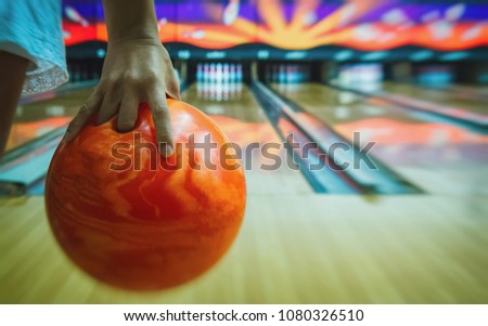 The human hand holds an orange bowling ball ready to throw it forward.