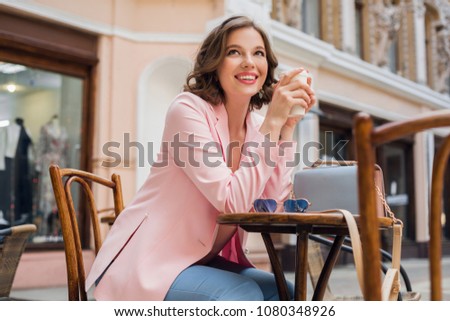 beautiful smiling woman in stylish outfit sitting at table wearing pink jacket, romantic happy mood, waiting for boyfriend on a date in cafe, spring summer fashion trend, drinking coffee