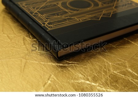 black leather photo book on golden background.
photobook with a shield on a  shinny  background. dark family photo album.wedding photoalbum.