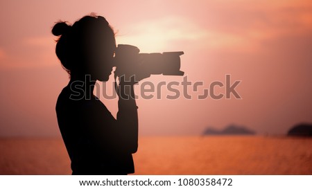 silhouette of young woman photographer, taking pictures of landscape at sunset