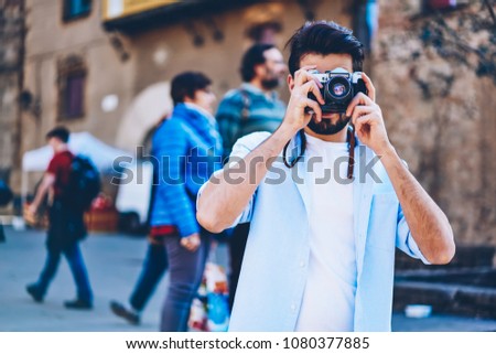 Man lover of travel focusing to take photos walking on streets of downtown during summer holiday.Tourist photographer making pictures on vintage camera with modern lenses strolling in urban setting