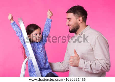 Father and her little daughter with thumbs up over pink background. Adult man and baby girl are happy