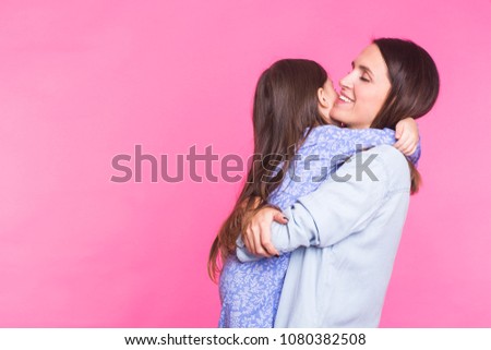 people, happiness, love, family and motherhood concept - happy little daughter hugging and kissing her mother over pink background with copyspace