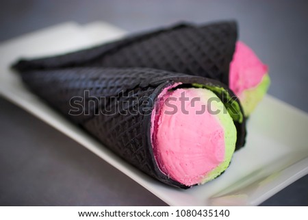 Bright pink-green ice cream in afashionable black cone. Soft focus.