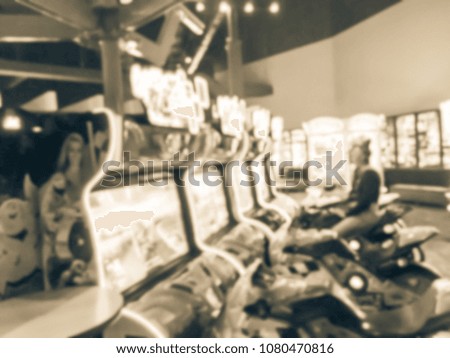 Blurred image dark room at entertainment complex in America, abstract arcade area with player on motorcycle racing simulator arcade game