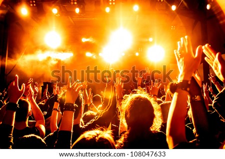 cheering crowd in front of bright yellow stage lights Royalty-Free Stock Photo #108047633