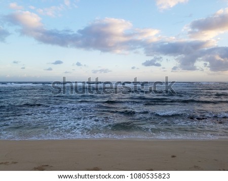 Waves of the ocean waters move towards the beach of Camp Mokuleia Beach looking into the pacific ocean with a clear blue sky on Oahu.