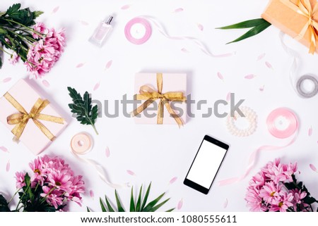 Festive composition of purple flowers, gift boxes with golden ribbons, mobile phone with blank screen and green leaves on a white table top view