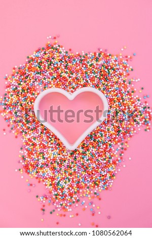 colored sugar sprinkles and baking shape heart on pink background. minimal creative design. sweets heart. symbol of love, romantic, Valentine's day. flat lay. copy space