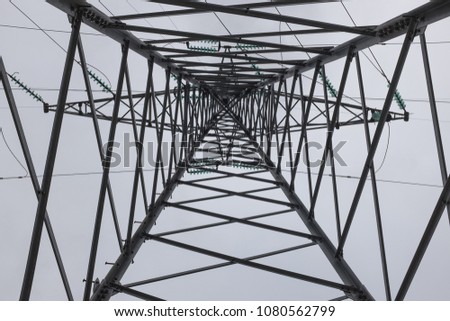 Electricity pylon pole post, shot from the ground up, high voltage metal construction with electric wires and cables, against a blown out white sky, geometric shape and pattern