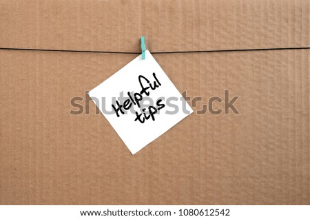 Helpful tips. Note is written on a white sticker that hangs with a clothespin on a rope on a background of brown cardboard