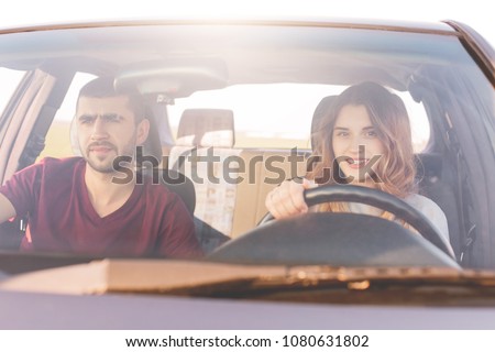 Couple travelers reach destination at car: beautiful smiling woman at wheel teaches to drive, her husband sits at front seat, controls everything. Girlfriend, boyfriend spend time together, have trip