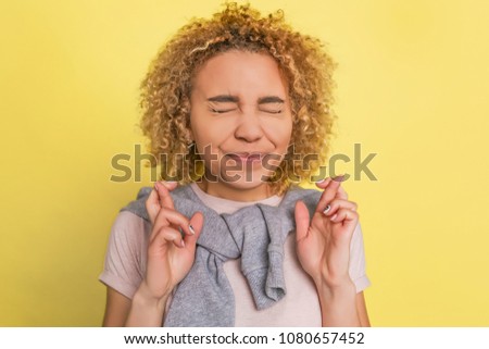 A gril is crossing her fingers. She is keeping her eyes closed. Isolated on yellow background