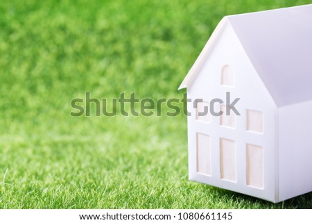 Hunting house concept. Model of white paper house on green grass background
