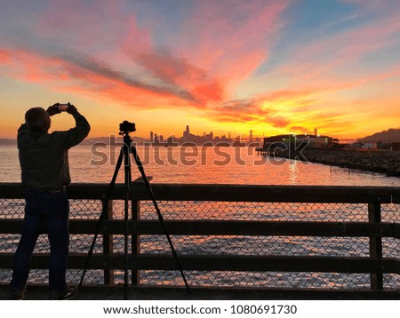 Photographer is taking a picture of sunset with San Francisco city silhouette, California, USA