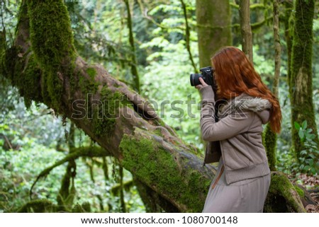 young girl with red hair is sitting on a tree branch with a camera and taking pictures